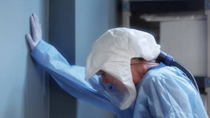 Meredith holding herself up against a wall while wearing full protective gear