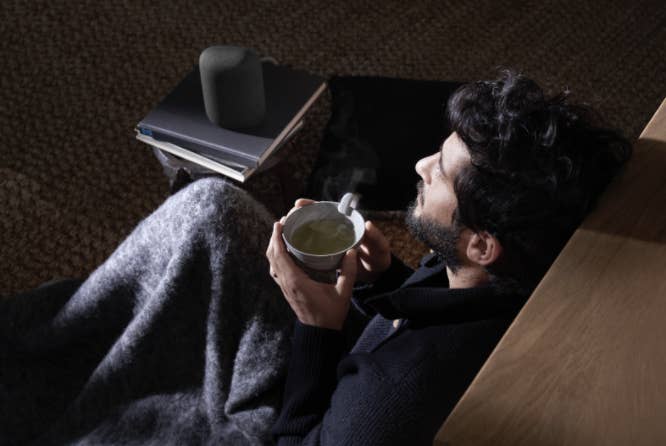 Man drinking tea on the couch next to a Google Nest