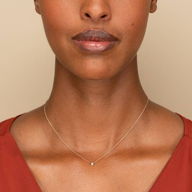 Small round diamond on a gold chain around a model's neck