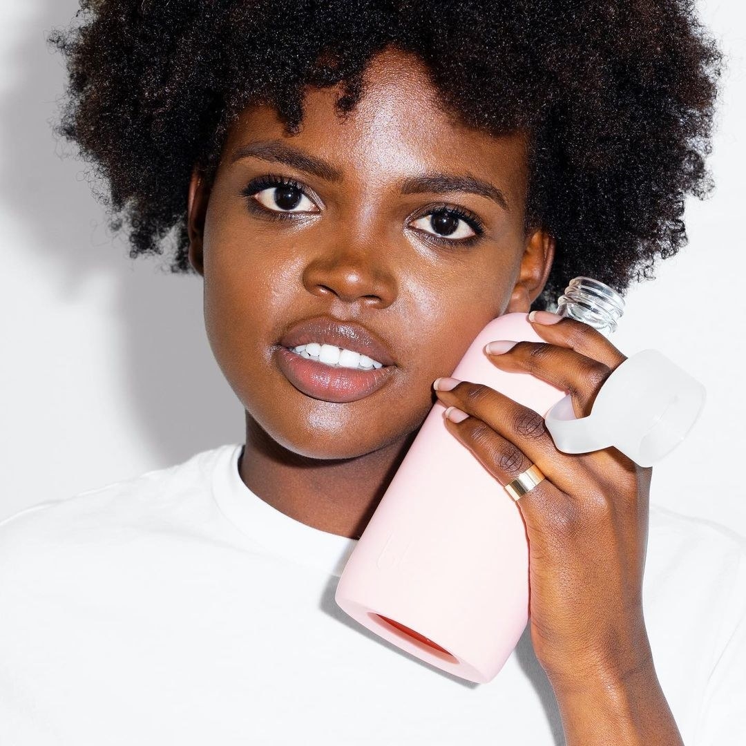Model holding the glass water bottle with a silicon pink cover on it and a lid by their face