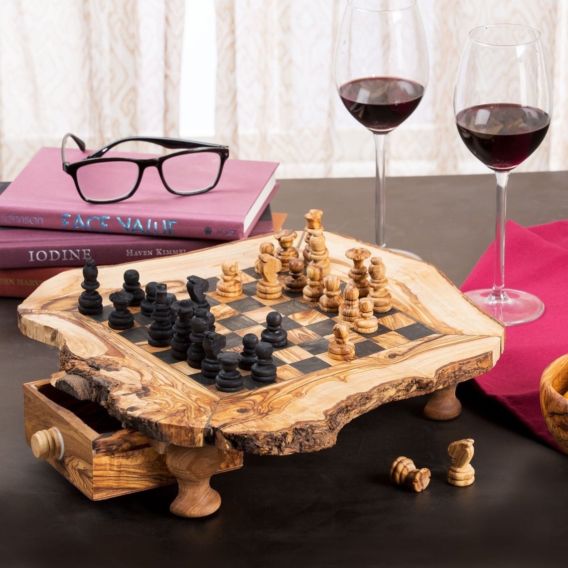 The chess board with pieces on top of it, there are wine glasses and books surrounding it