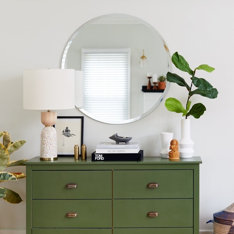 Round frameless mirror mounted on wall above dresser