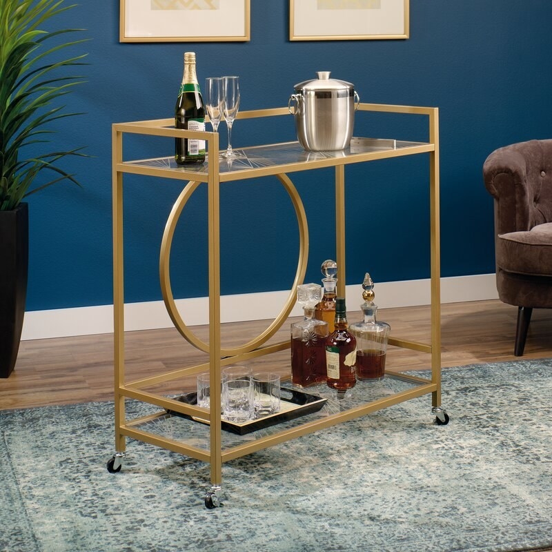 Gold bar cart on wheels with glasses and alcohol on the shelves