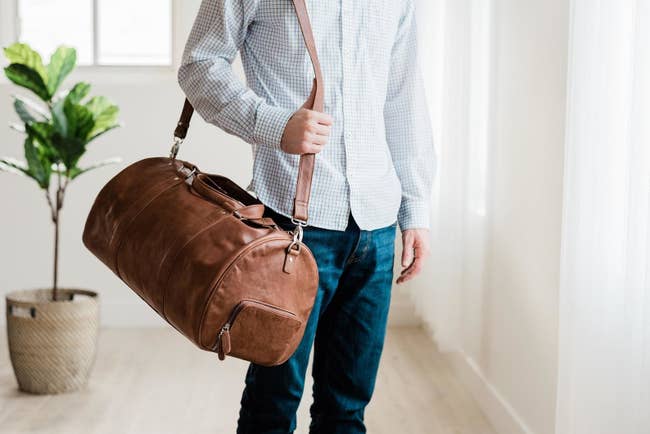 The oval-shaped brown leather bag with a long shoulder strap over a model's shoulder