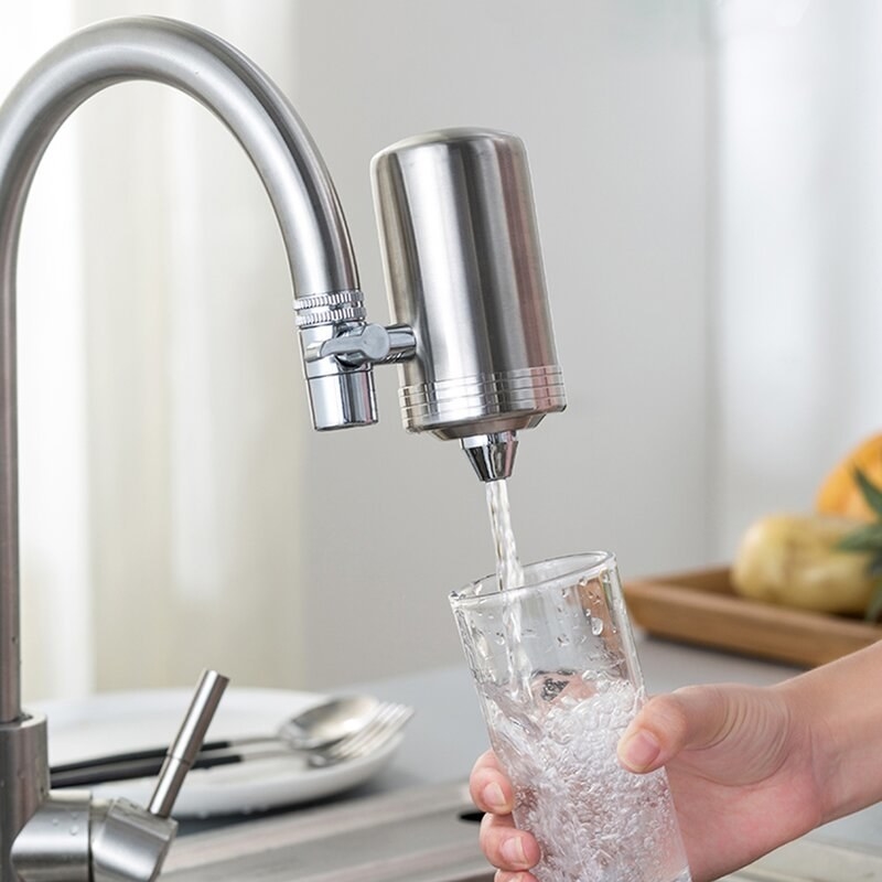 a silver water filter attached to a faucet, filling a drinking glass