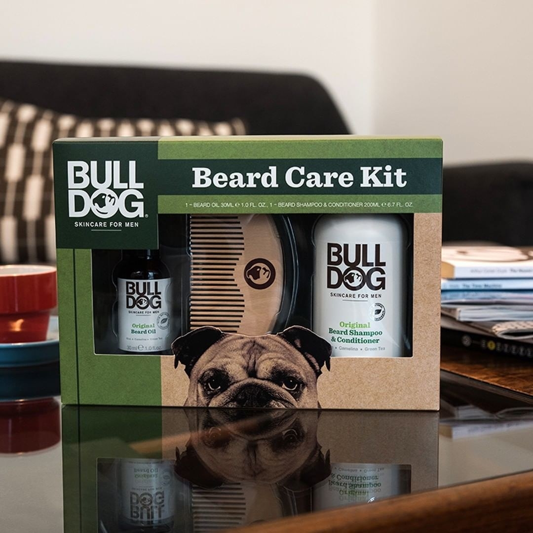 The boxed set of beard oil, shampoo, and comb on a coffee table next to a stack of magazines