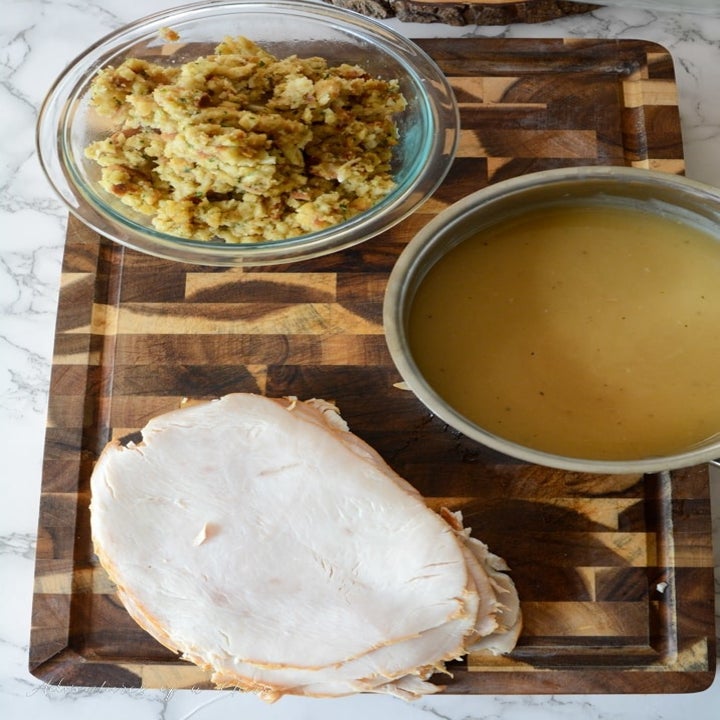Deli turkey slices, gravy, and stuffing on a cutting board.