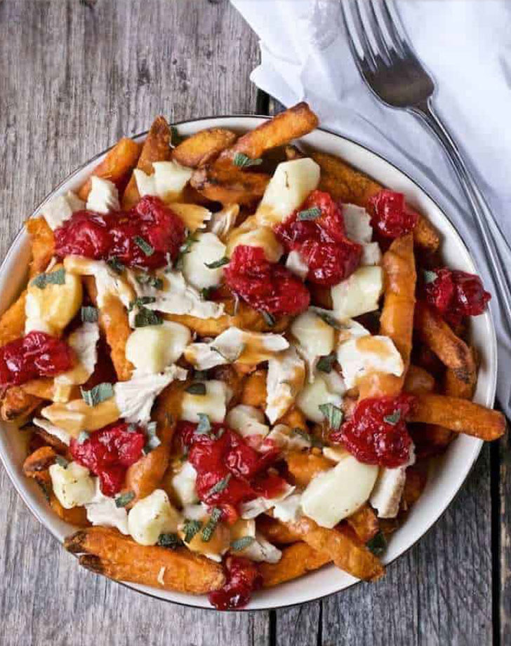 A plate of sweet potato fries poutine topped with cheese curds, cranberry sauce, turkey, and gravy.