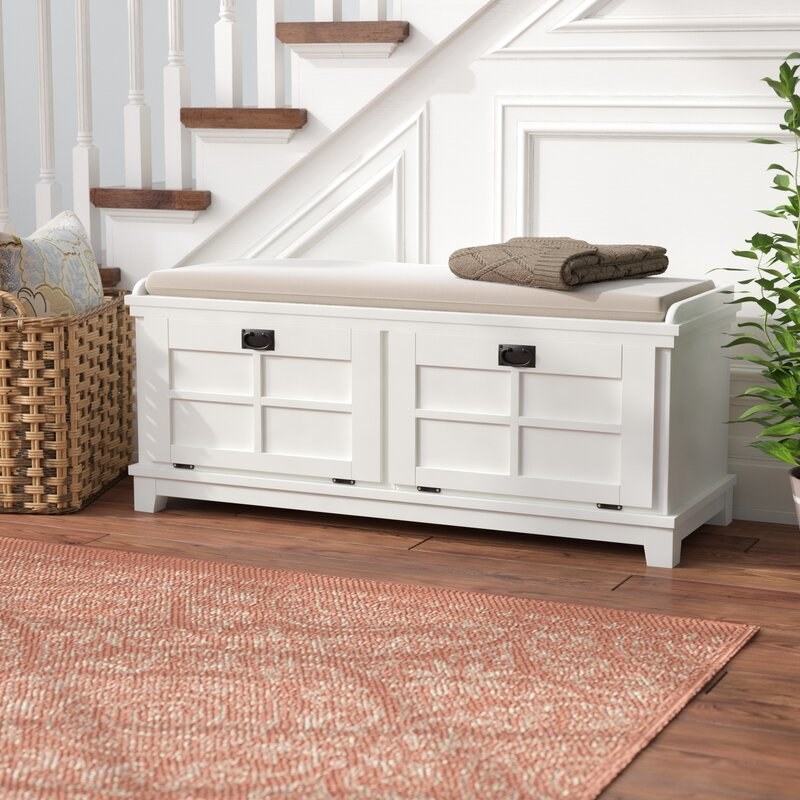 a white storage bench with a tan cushion on top in a hallway
