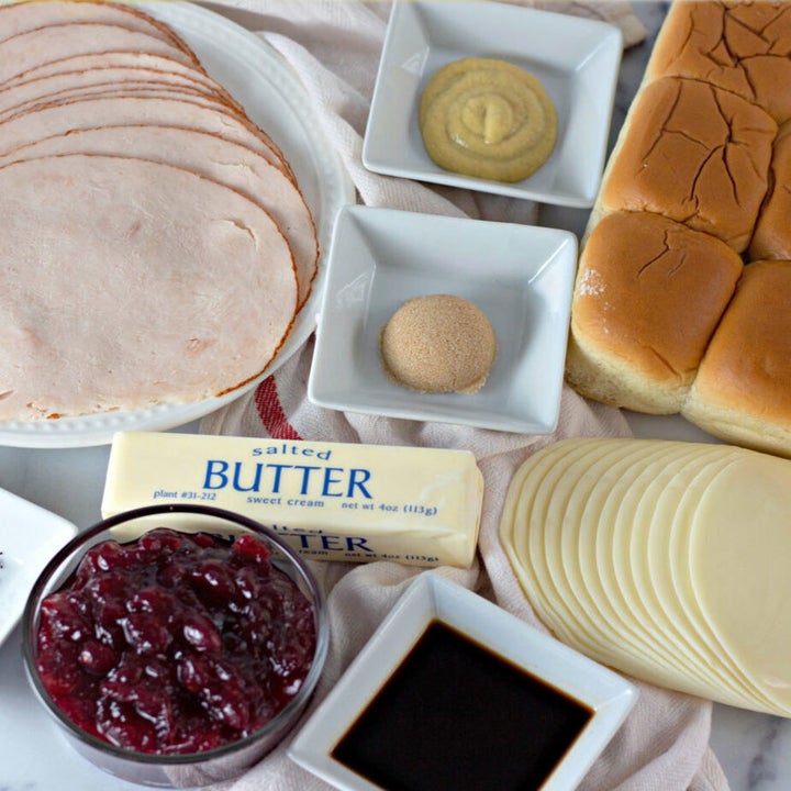 Ingredients for turkey sliders including deli meat, cranberry sauce, rolls, provolone cheese, and butter.