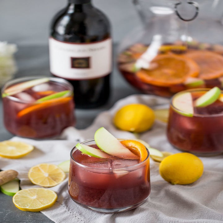 Three glasses and a pitcher of sangria with a bottle of Two Buck Chuck.