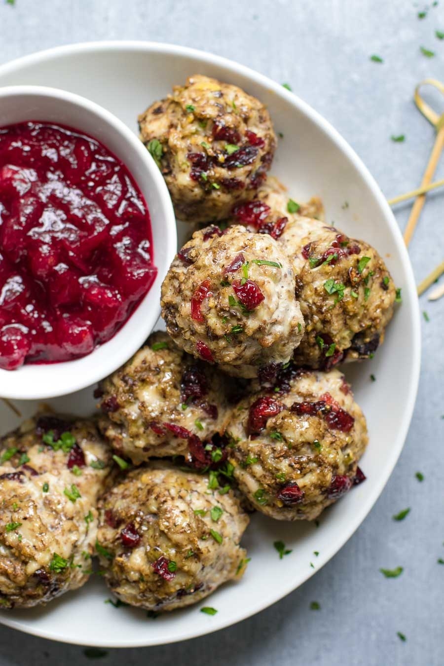 A plate of turkey meatballs with cranberries, fresh herbs, and cranberry sauce for dipping.
