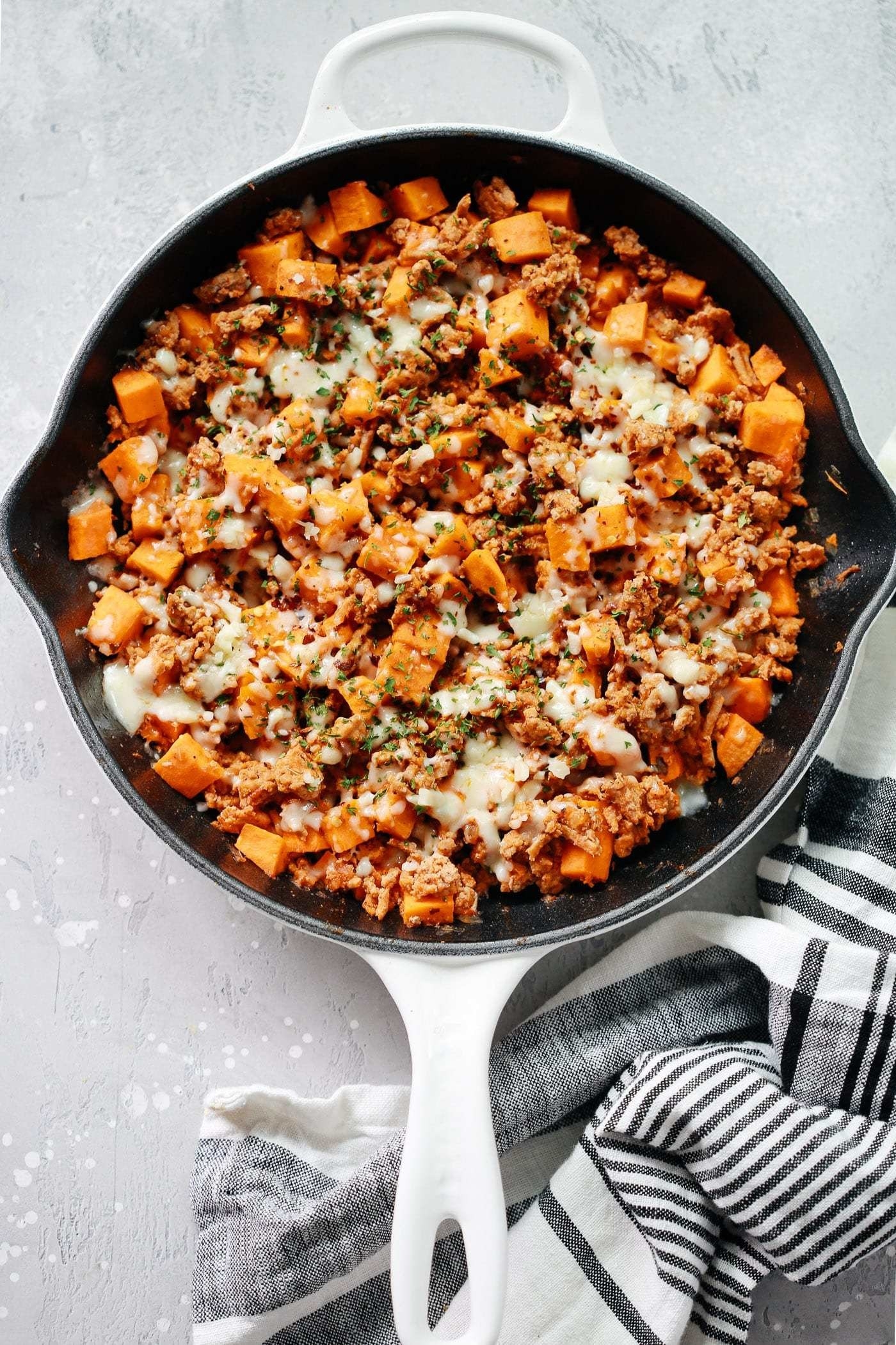A skillet filled with turkey, sweet potatoes, and cheese.