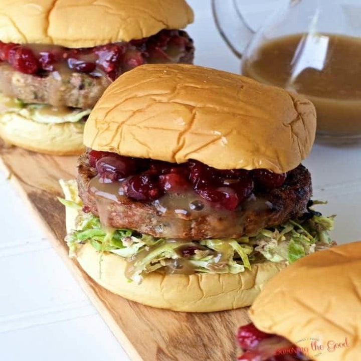 Three turkey burgers with cranberry sauce and Brussels sprout slaw on buns.