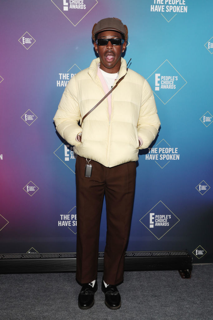 Tyler, the Creator wears a puffy jacket, newsboy cap, slacks, loafers, and sunglasses