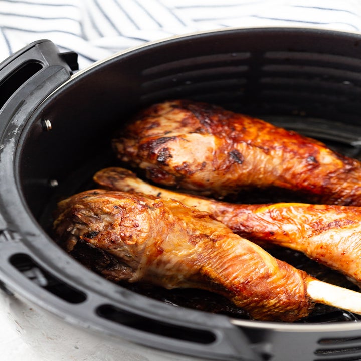 Three crispy skinned turkey legs in the basket of an air fryer.