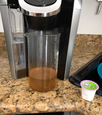Reviewer's beaker beneath Keurig showing the effects of cleaning pods with brown water coming out of machine.