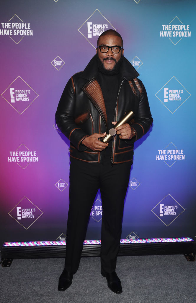 Tyler Perry wears a leather jacket with brown detailing over an all-black ensemble and his signature glasses