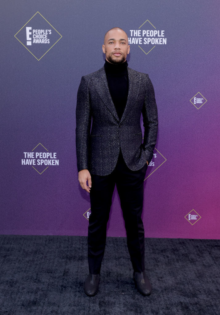 Kendrick Sampson wears a textured blazer over an all-black ensemble of a turtleneck and slacks