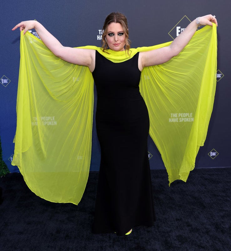 Lauren Ash wears a gown with a contrasting floor-length scarf that she holds out like bat wings