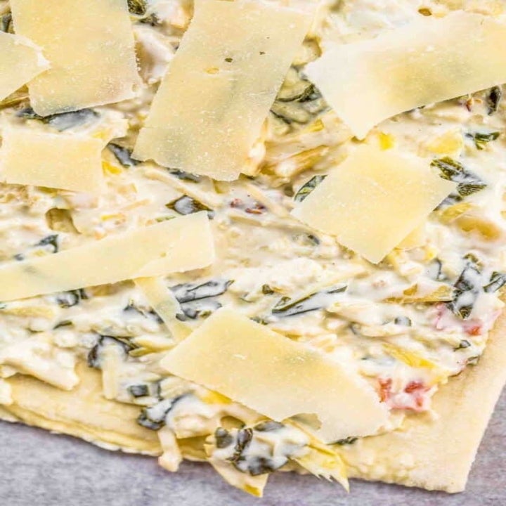 Puff pastry dough topped with spinach artichoke dip and Parmesan cheese.