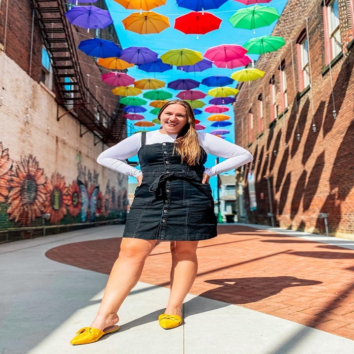 A reviewer wearing the mid-thigh, button front dress in dark denim over a long sleeved top
