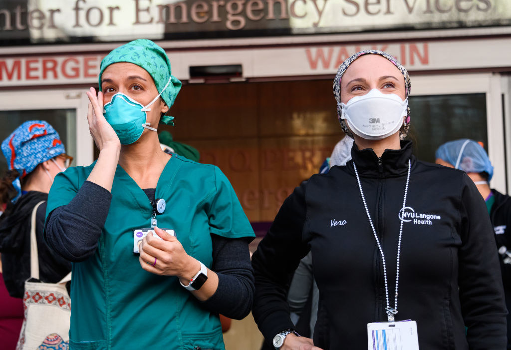 Two medical professionals, one who is wiping away tears from their eyes, standing next to one another