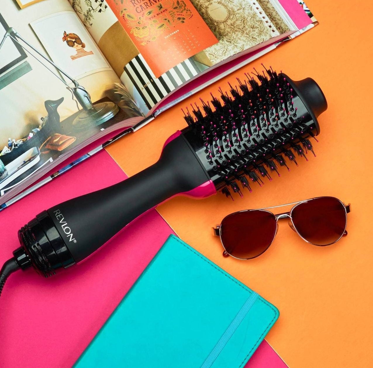 The Revlon hair dryer in black and pink beside a journal, sunglasses, and a magazine