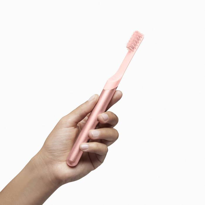The quip metal toothbrush in pink held in a hand to show its size