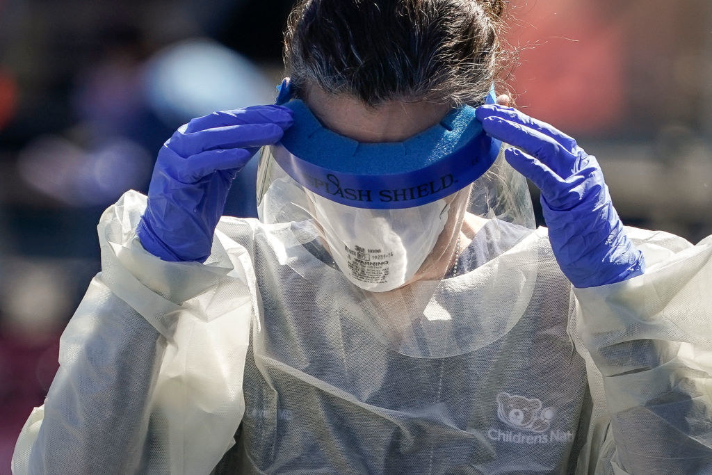 A medical professional adjusting their protective face shield over her face mask