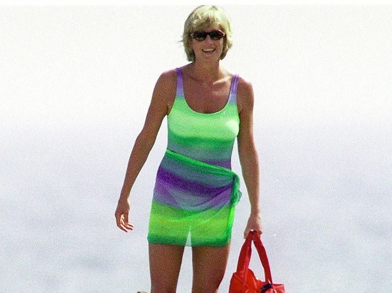 Princess Diana smiling in a bathing suit, a coverup tied around her waist, and sunglasses