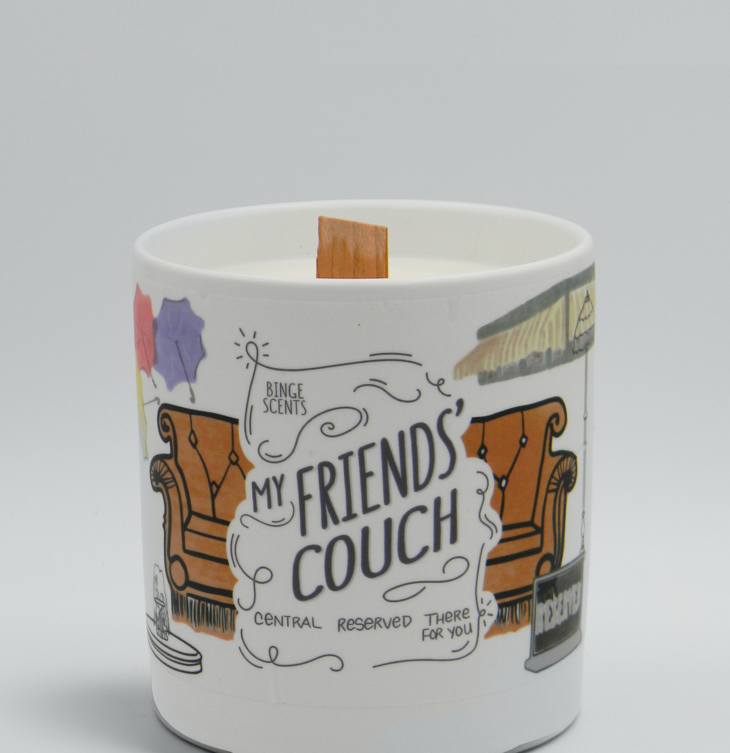 The candle with an illustration of a brown couch, and other illustrations from the show around it and the words &quot;My Friends&#x27; Couch&quot; on it