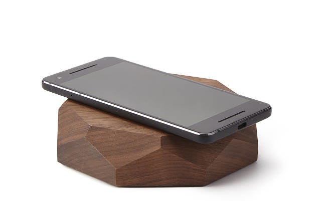 A smartphone resting on a geometric walnut wood charger with a flat top 