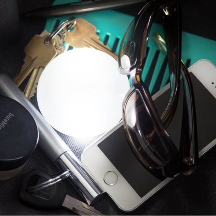 The small round light illuminating a phone, sunglasses, and other common purse contents 