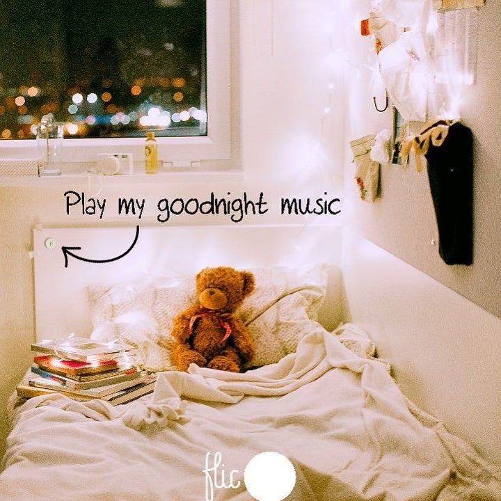 A teddy bear and a pile of books sitting on a bed with a flic button mounted on the headboard and an arrow pointing to it with text that reads "Play my goodnight music" 