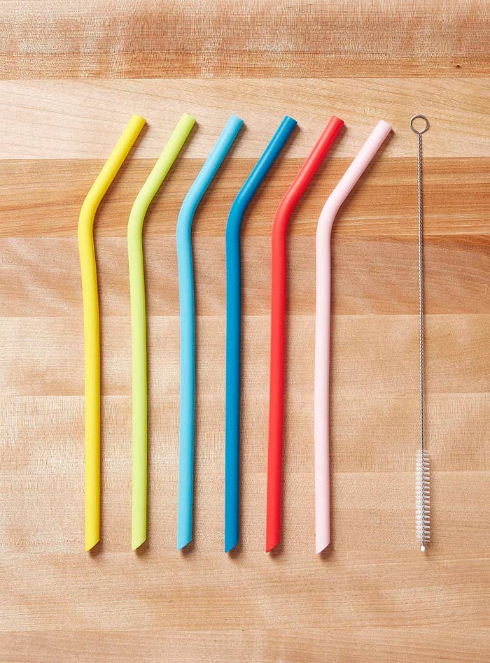 Six silicone straws on a wooden table with a small cleaning brush next to them