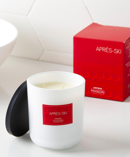 A close up of a candle on a simple surface, with a label that says Apres Ski