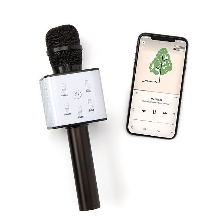 A karaoke microphone with several control buttons sitting next to a smartphone