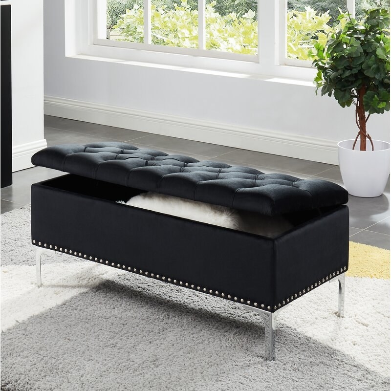 A black, velvet, upholstered storage bench with a flip-top lid and chrome legs