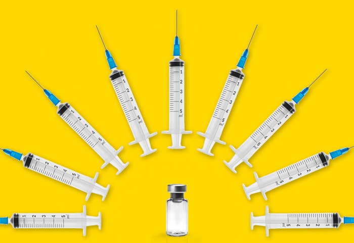 Several syringes arc over a vaccine vial.