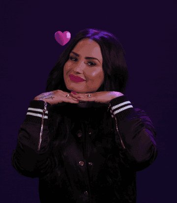 GIF of Demi resting her head on her hands and making a cute face as hearts float around her