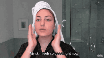 Woman in a bathrobe and towel on her hair, patting her skin and saying ‘My skin feels so good right now.’