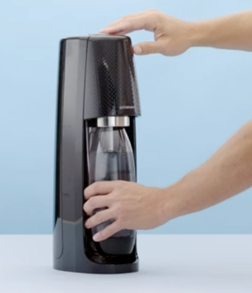 Person detaching a bottle, now filled with sparkling water, from the SodaStream machine