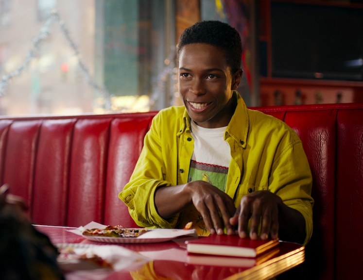 Boomer sits in a booth at the pizza place he works at with his hands on a red notebook