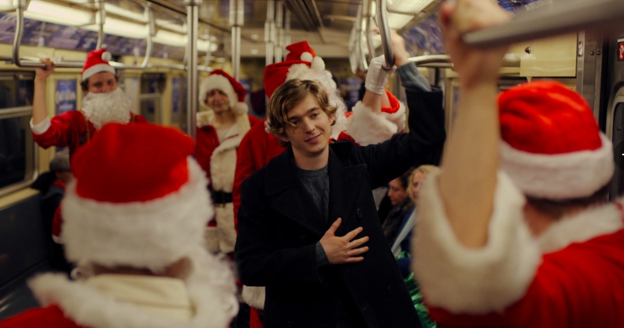 Dash stands on a subway car full of people in Santa costumes