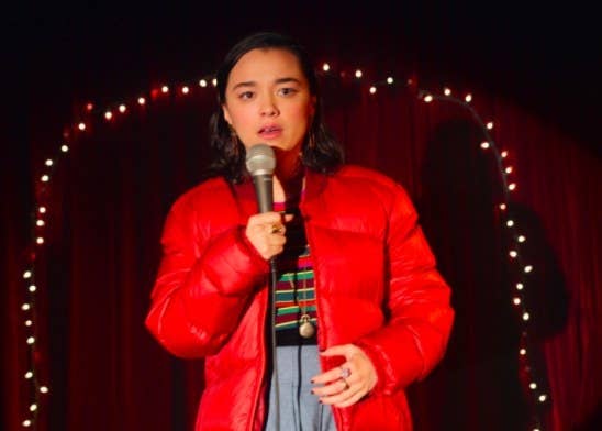 Lily stands on stage with fairy lights on the curtain behind her, holding a microphone