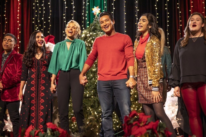 A group of people stand holding hands on a stage covered in Christmas decorations