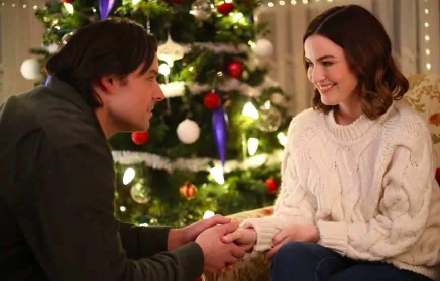 Jonna Walsh and Jesse Hutch shake hands while seated in front of a Christmas tree