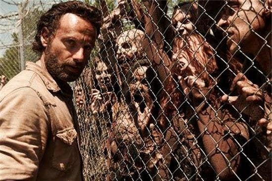 A man standing before a fence with zombies on the other side struggling to get to him.