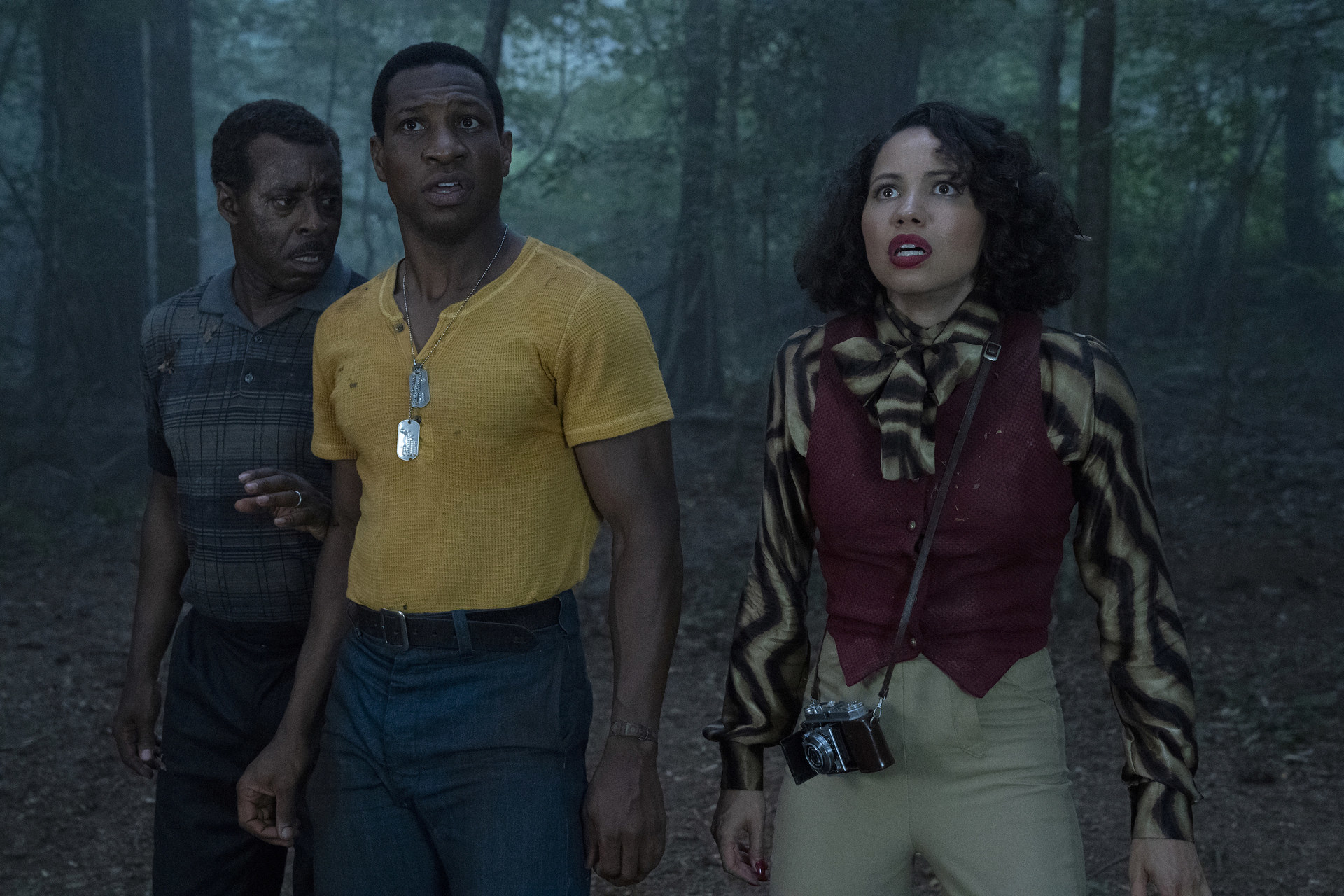 Two men and a woman looking terrified in a forrest.
